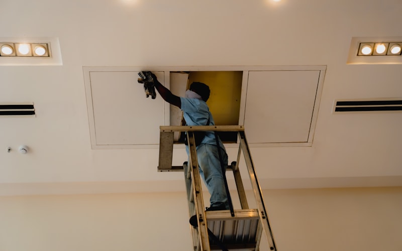 Technician working on ceiling access panel for duct maintenance